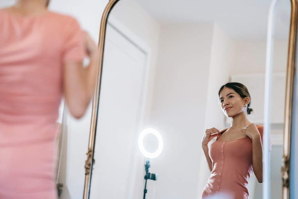 A young woman poses confidently in front of a mirror with a ring lamp.