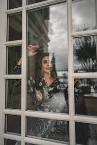 Fashionable woman standing behind a window, reflecting urban Istanbul architecture.