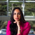 Portrait of a confident woman in a stylish pink suit, sitting indoors.