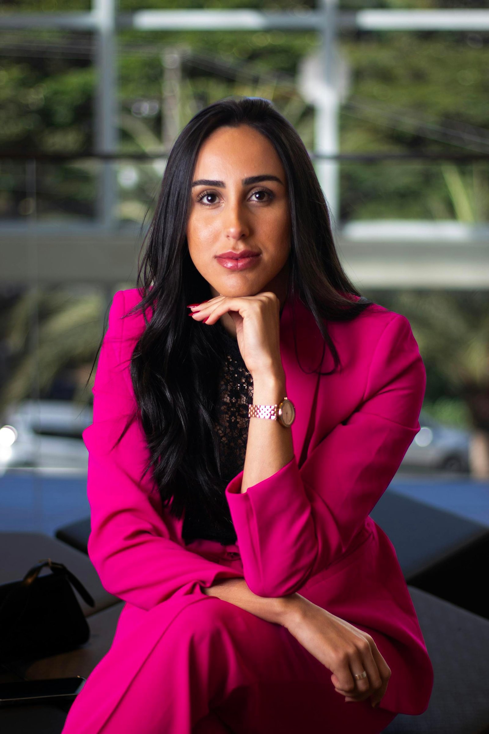 Portrait of a confident woman in a stylish pink suit, sitting indoors.