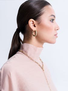 Stylish portrait of a woman wearing gold hoop earrings and chain necklace.