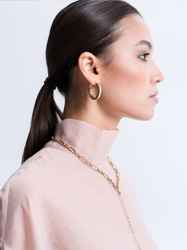 Stylish portrait of a woman wearing gold hoop earrings and chain necklace.
