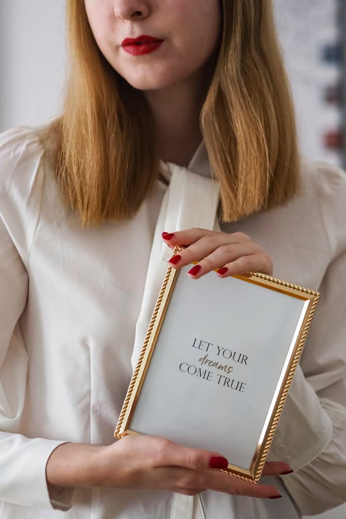 Woman holding a frame with the quote 'Let your dreams come true' in elegant attire.